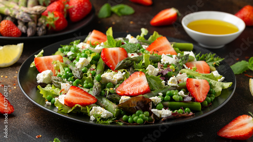 Asparagus and Strawberry Salad with vegetables, green peas and feta cheese in black plate. healthy food.