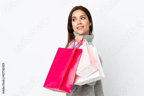 Young caucasian woman isolated on white background holding shopping bags and looking back