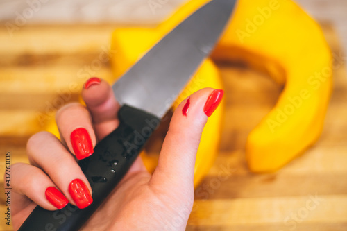 Female hand with red manicure holds knife with wounded hand, on background of cutting board with pumpkin