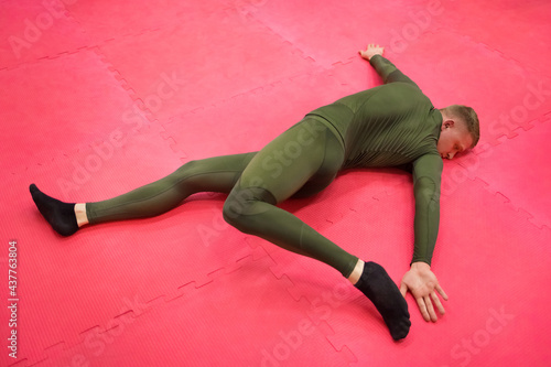 Young sports guy in a green thermal suit does exercises on the gym floor