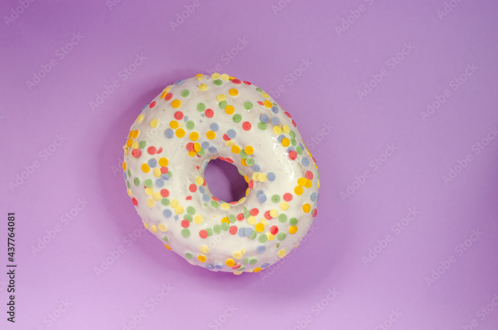 Donut in white glaze and round multi-colored balls on an lilac background Donut in white glaze and round multi-colored balls on an lilac background