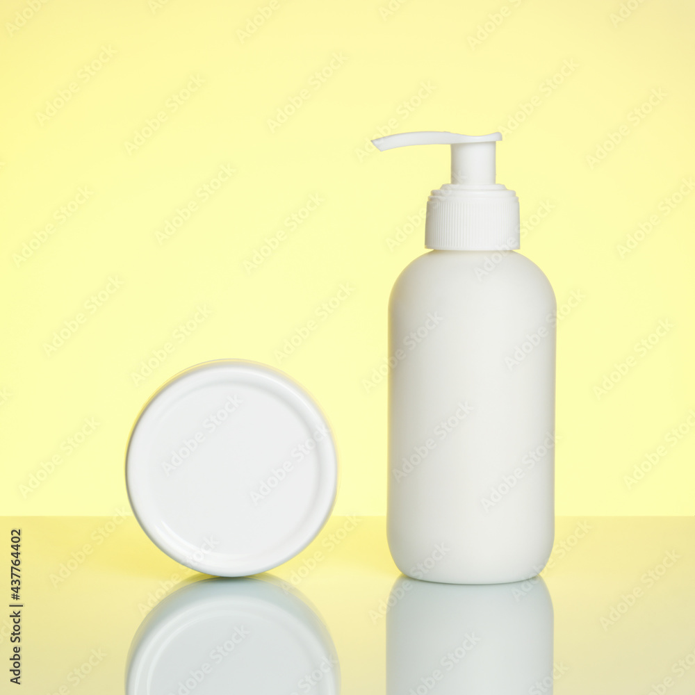 Hand cream in a bottle and jar on a yellow background with reflection. Hand cream in a bottle and jar on a yellow background with reflection.