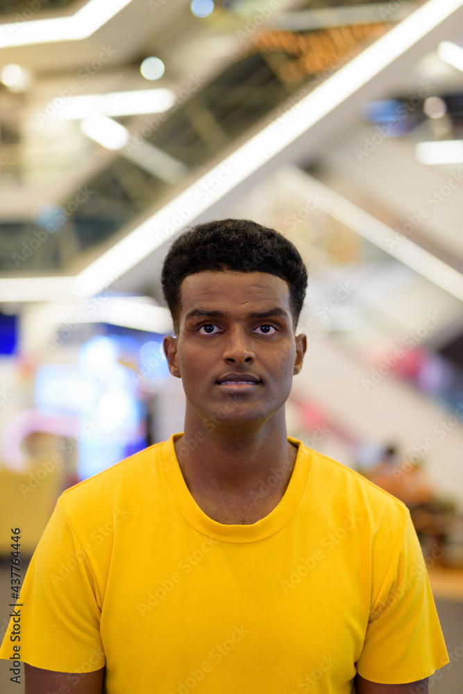Vertical portrait of handsome black African man wearing yellow t-shirt in shopping mall Vertical portrait of handsome black African man wearing yellow t-shirt in shopping mall