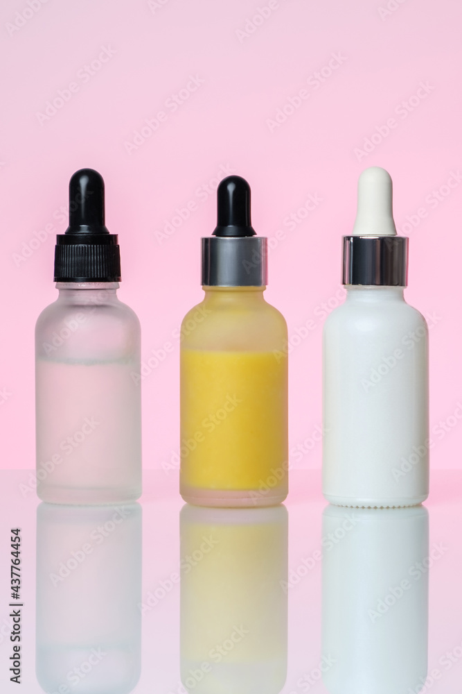 Three bottles of serum on a light pink background. Moisturizer, vitamin C, hyaluronic acid. Three bottles of serum on a light pink background. Moisturizer, vitamin C, hyaluronic acid.