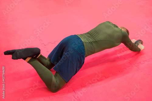 Young sports guy in a green thermal suit does exercises on the gym floor