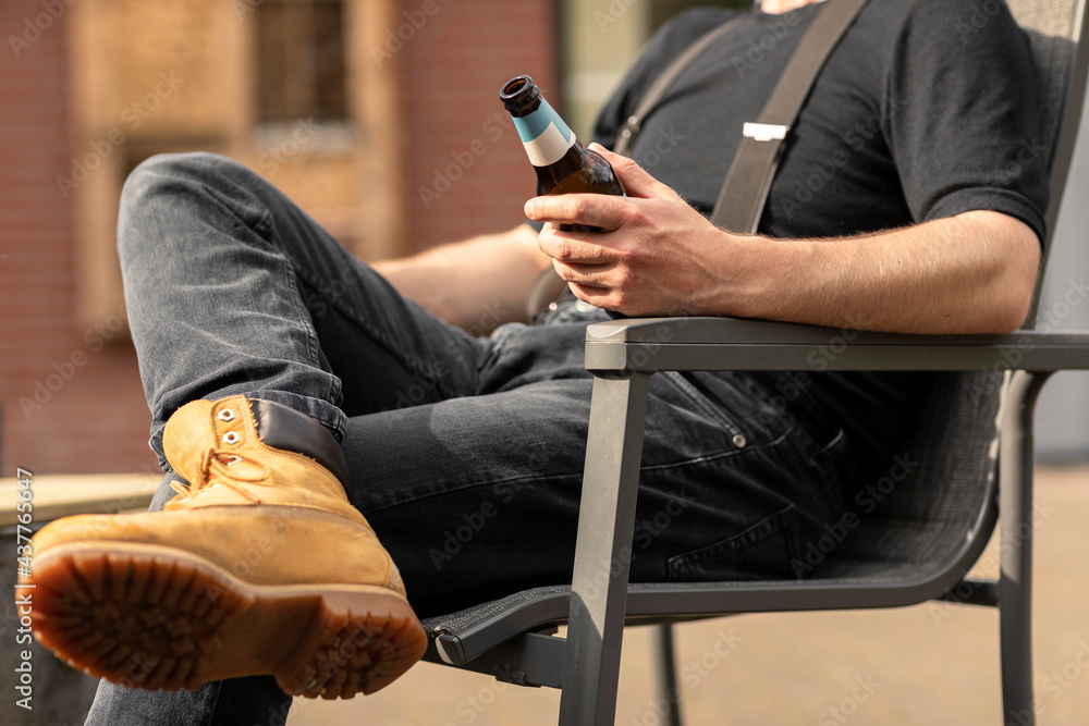 A man holding a beer bottle while sitting in the sun and having a break, relaxing and enjoying the simple life A man holding a beer bottle while sitting in the sun and having a break, relaxing and enjoying the simple life