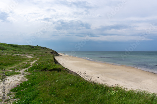 hiking trail leads through tall grassy sand dunes to a secluded and empty white sand beach with a calm turquoise ocean behind