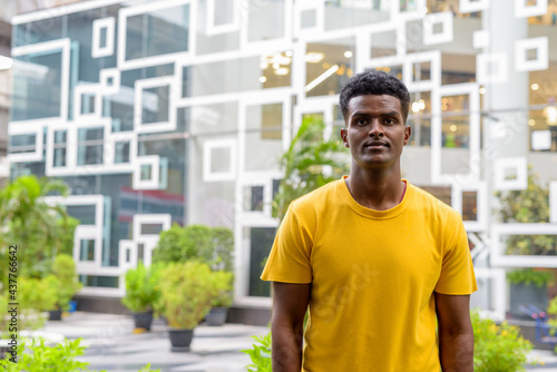 Portrait of handsome black African man wearing yellow t-shirt outdoors in city during summer
