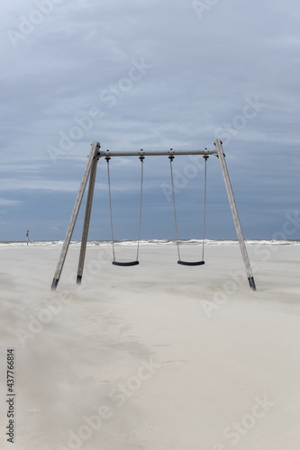 two swings on an empty golden sand beach with the Wadden Sea of northern Germany in the background