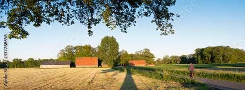 Fotografie man on bicycle near old barns and farm at sunset in rural area of twente near ol