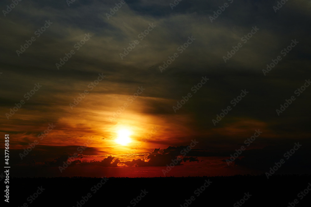 beautiful sunset sky, bright sun and dark silhouette of clouds as a background