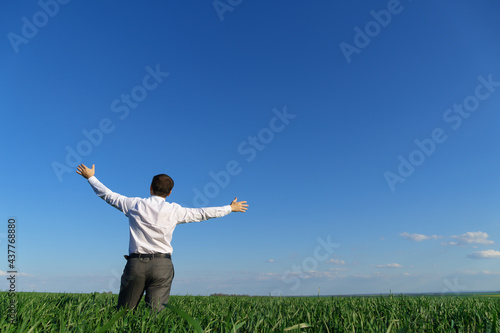 businessman poses in a field, he looks into the distance and rests, green grass and blue sky as background