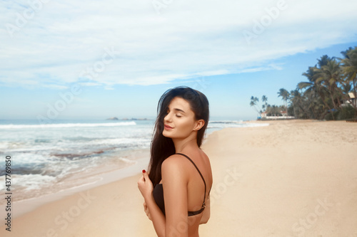 Portrait of fashion young girl with tanned sexy body. Beautiful woman in black bikini on tropical beach. Skine care photo