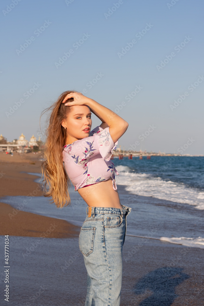 Young beautiful woman with long hair standing on the beach in top and jeans. Vacation summer concept Young beautiful woman with long hair standing on the beach in top and jeans. Vacation summer concept