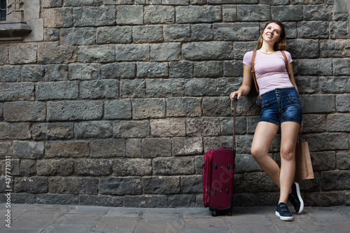 cheerful young woman with travelling bag on stone wall background outdoors