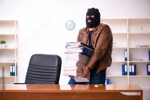 Young man in balaclava stealing information from the office