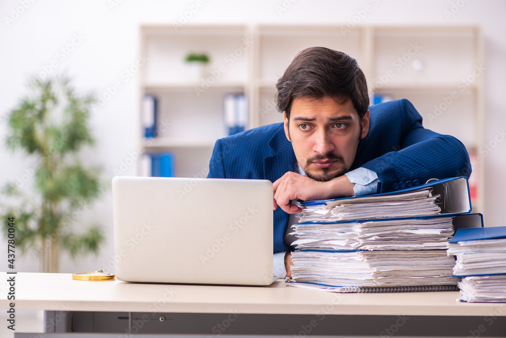 Young male employee unhappy with excessive work in the office Young male employee unhappy with excessive work in the office