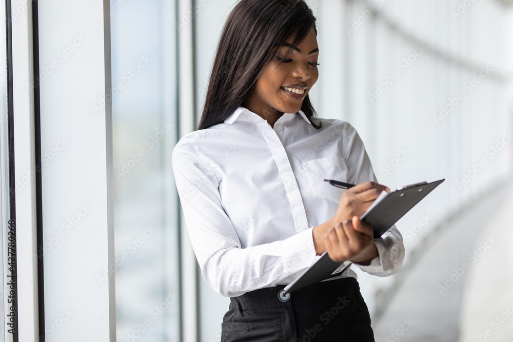 African american businesswoman talking on mobile phone and holding clipboard in office African american businesswoman talking on mobile phone and holding clipboard in office