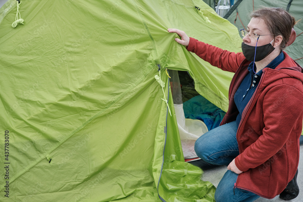 Middle aged caucasian woman wearing glasses and a mask against the virus chooses a large tent in the store for tourism and outdoor activities