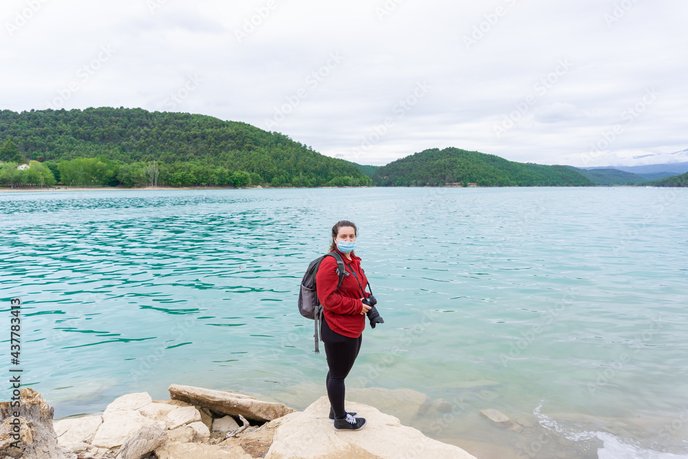 Woman on the shore of a lake with blue protective mask, holding a camera