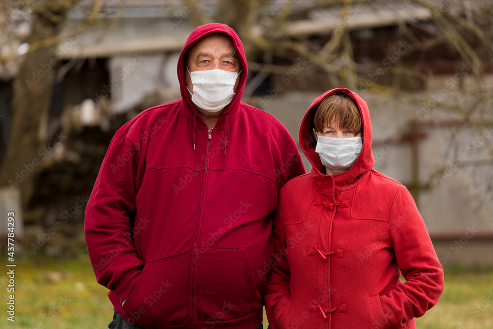 An elderly man and woman Caucasian or European hooded look stand next to each other in an open-air street, in protective safe medical masks against coronavirus An elderly man and woman Caucasian or European hooded look stand next to each other in an open-air street, in protective safe medical masks against coronavirus