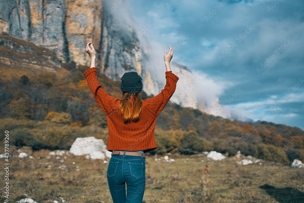 Obraz premium woman in a sweater and jeans with raised up arms travels in the mountains on nature landscape