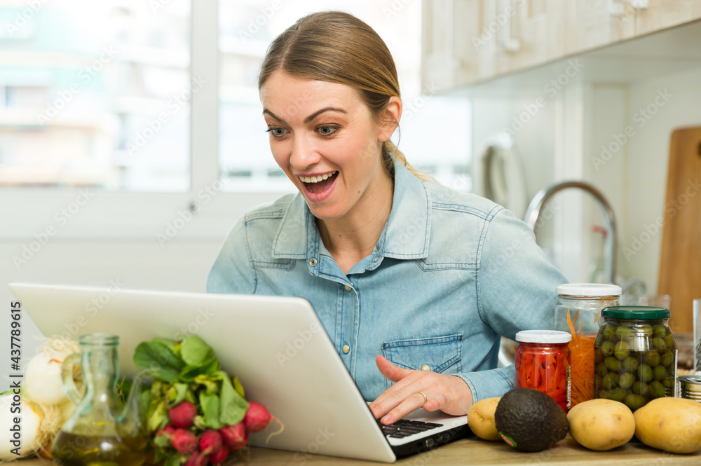 Portrait of enthusiastic young woman sitting with laptop at home kitchen