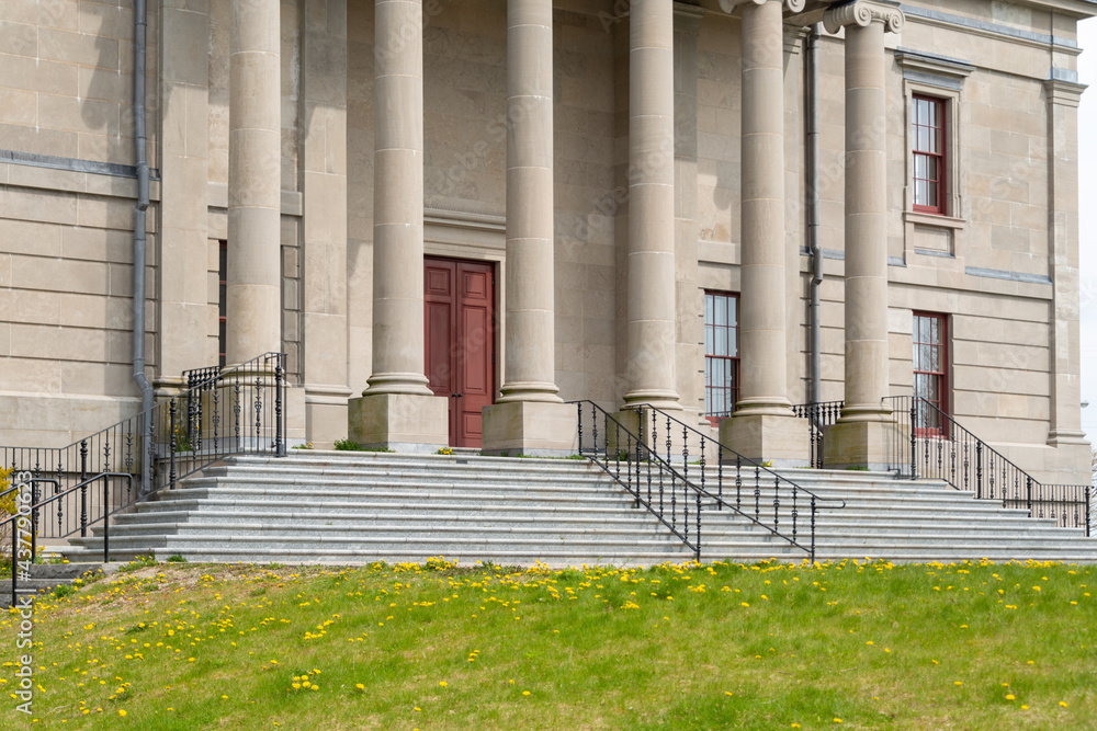 A wide brick entrance to a large courthouse, justice or government style building. There's a tall red door, grey marble steps, black handrails, tall windows, round pillars and a beige exterior wall. A wide brick entrance to a large courthouse, justice or government style building. There's a tall red door, grey marble steps, black handrails, tall windows, round pillars and a beige exterior wall.