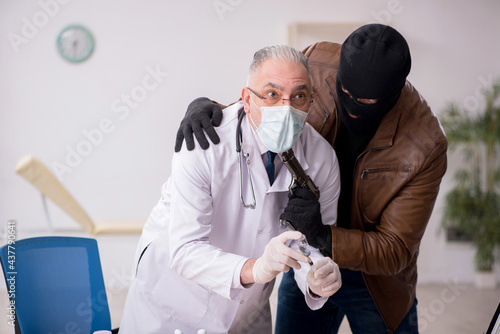 Masked man burglar stealing vaccine from old doctor photo