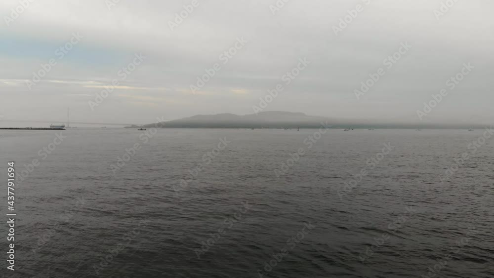 Flying low over calm seas towards distant misty island Flying low over calm seas towards distant misty island
