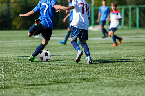 Fototapeta Naklejka Na Ścianę i Meble -  Young sport boys in blue sportswear running and kicking a  ball on pitch. Soccer youth team plays football in summer. Activities for kids, training	