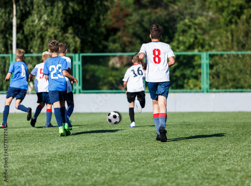Young sport boys in blue sportswear running and kicking a ball on pitch. Soccer youth team plays football in summer. Activities for kids, training 