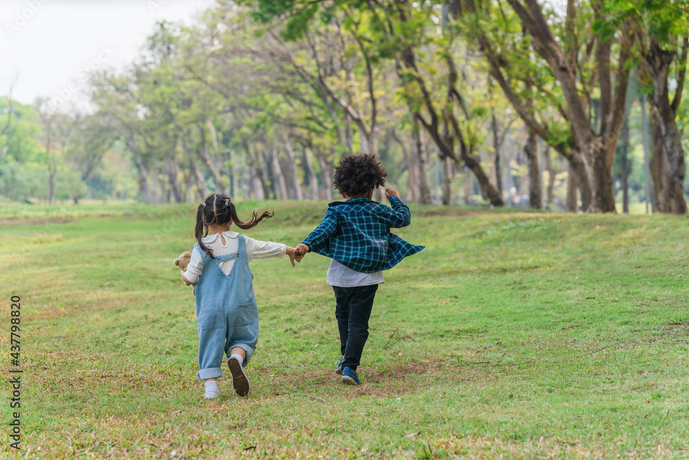 two diverse mixed race children playing and running together in park