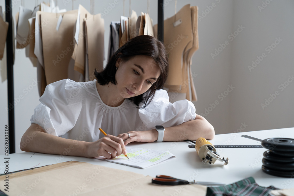 Young female fashion designer make notes of measurements plan new collection in sewing studio workshop Creative seamstress, freelance tailor writing idea for trendy clothes concept. Girl sewer at work