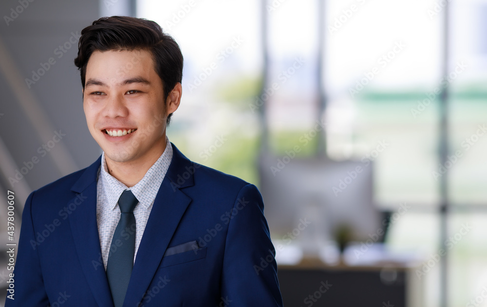 young attractive asian business man wearing navy blue suit with white shirt and necktie smiling beautifully looking in the future in office with natural lighting young attractive asian business man wearing navy blue suit with white shirt and necktie smiling beautifully looking in the future in office with natural lighting