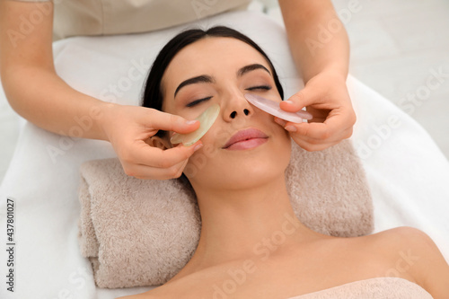 Young woman receiving facial massage with gua sha tools in beauty salon photo