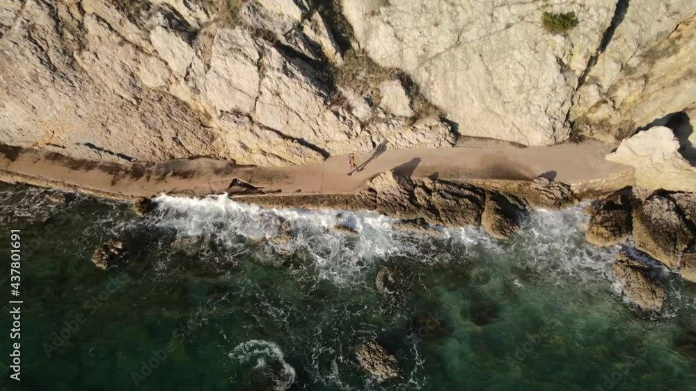 Aerial reverse shot panning up with drone on the coast of Beska in Croatia with a woman walking next to mountain and the adriatic sea Aerial reverse shot panning up with drone on the coast of Beska in Croatia with a woman walking next to mountain and the adriatic sea