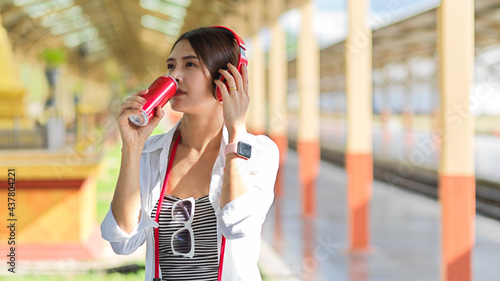 Portrait of female traveller with headphones drinking beverage can in train station