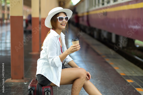 Side view of female traveler with hat and sunglasses holding paper cup at train station