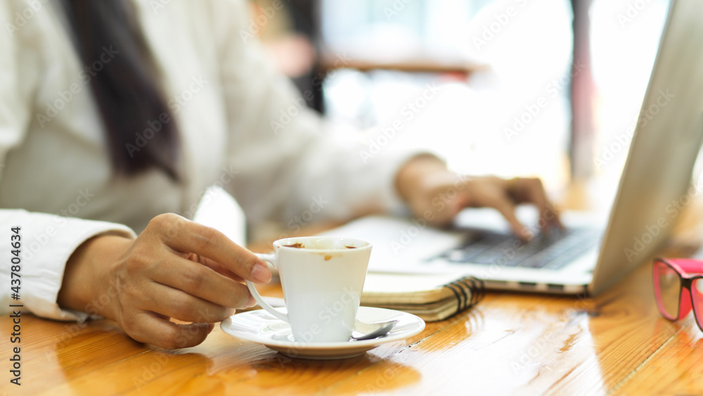 Close up view of female hand holding coffee cup while working with laptop Close up view of female hand holding coffee cup while working with laptop