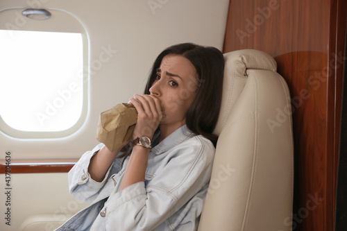 Nervous young woman with aviophobia breathing into paper bag in airplane photo