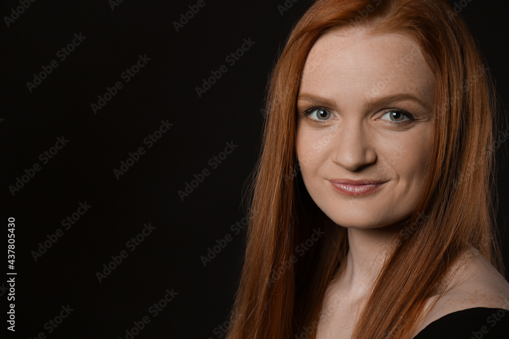 Candid portrait of happy young woman with charming smile and gorgeous red hair on dark background, space for text Candid portrait of happy young woman with charming smile and gorgeous red hair on dark background, space for text
