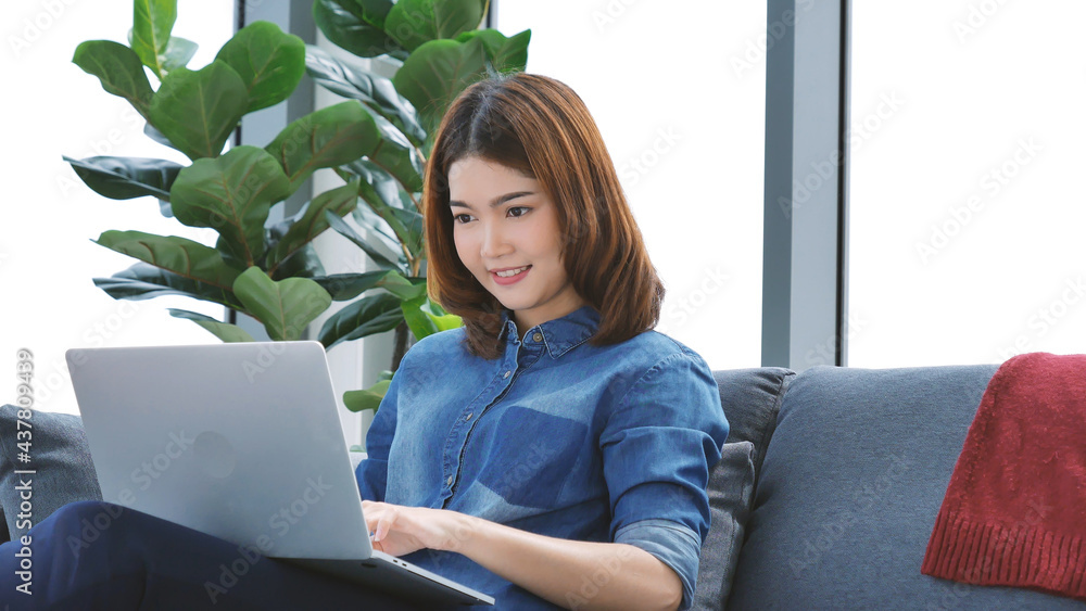 Woman working from home on laptop online meeting in home office. Entrepreneur asian business woman using notebook laptop sit on sofa technology new normal lifestyle. Happy woman typing keyboard laptop