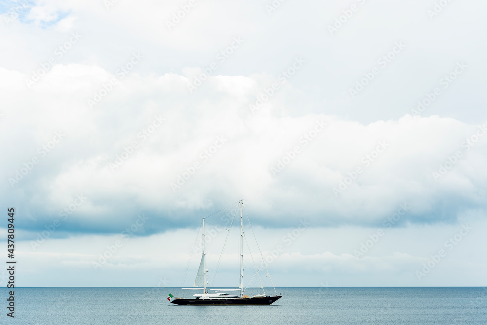 Stunning view of a luxury sailboat sailing on a beautiful calm sea during a dramatic, cloudy day. Costa Smeralda, Sardinia, Italy. Recreational pursuit, copy space.