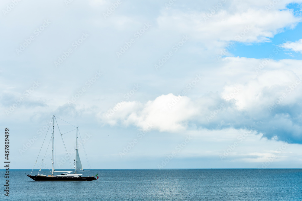Stunning view of a luxury sailboat sailing on a beautiful calm sea during a dramatic, cloudy day. Costa Smeralda, Sardinia, Italy. Recreational pursuit, copy space.