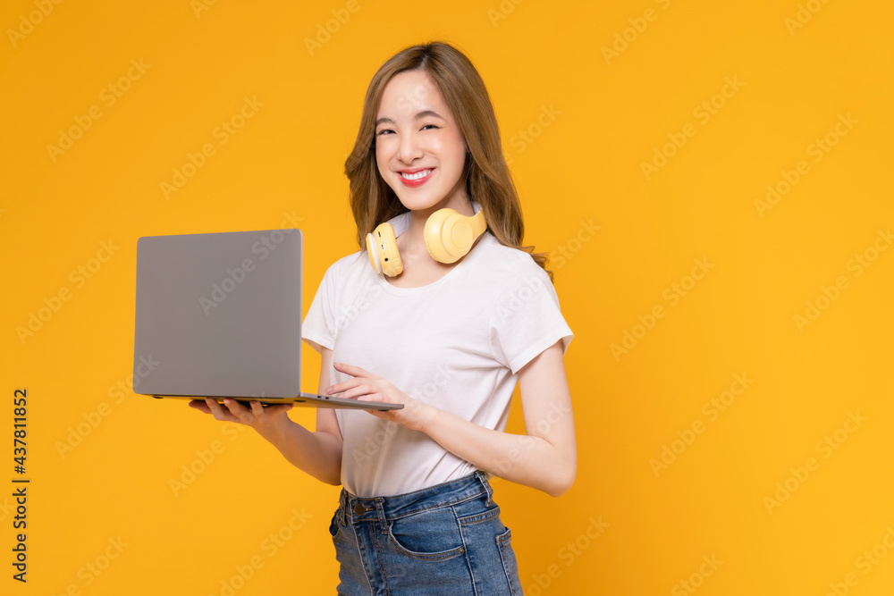 Studio shot of cheerful beautiful Asian woman in white t-shirt and holding laptop mockup of blank screen on yellow background. Studio shot of cheerful beautiful Asian woman in white t-shirt and holding laptop mockup of blank screen on yellow background.