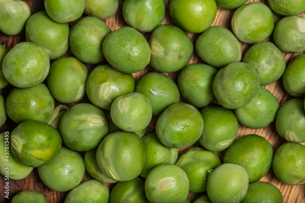 Top view Fresh raw green peas (Pisum sativum) in a wooden bowl with leaves and flower on a wooden table