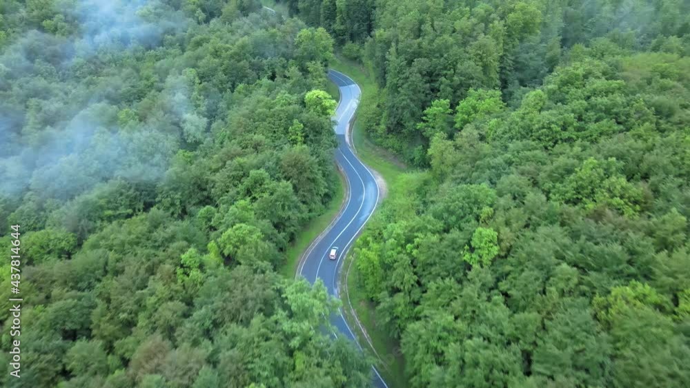 Aerial drone view following a Electric car, driving on a foggy forest road Aerial drone view following a Electric car, driving on a foggy forest road