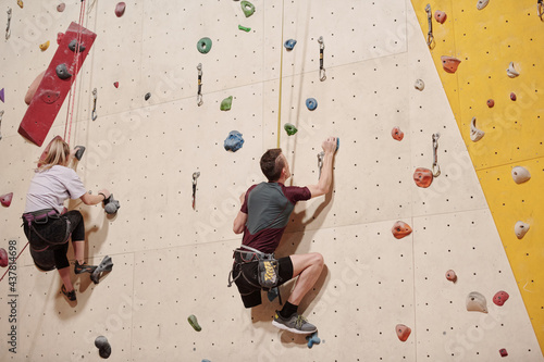 Young disable man and blond girl climbing wall during training