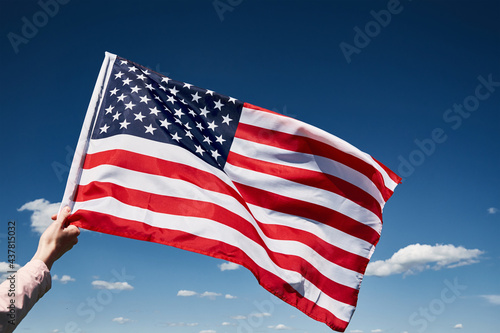 Waving american flag outdoors. Hand holds usa national flag against blue cloudy sky. 4th July Independence Day